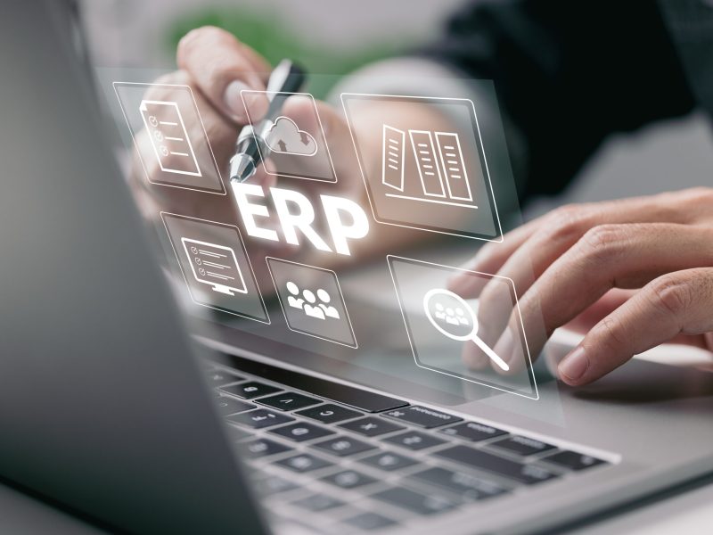 Enterprise Resource Planning (ERP) is a business resource planning software system. On a virtual screen, there is a concept of a hand typing computer laptop icons.